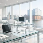 Helles Büro mit Glaswänden, Blick auf Wasser und Stadt. Schreibtisch mit Laptop, Tasse, Stift, Mouse und Aktenordner.
